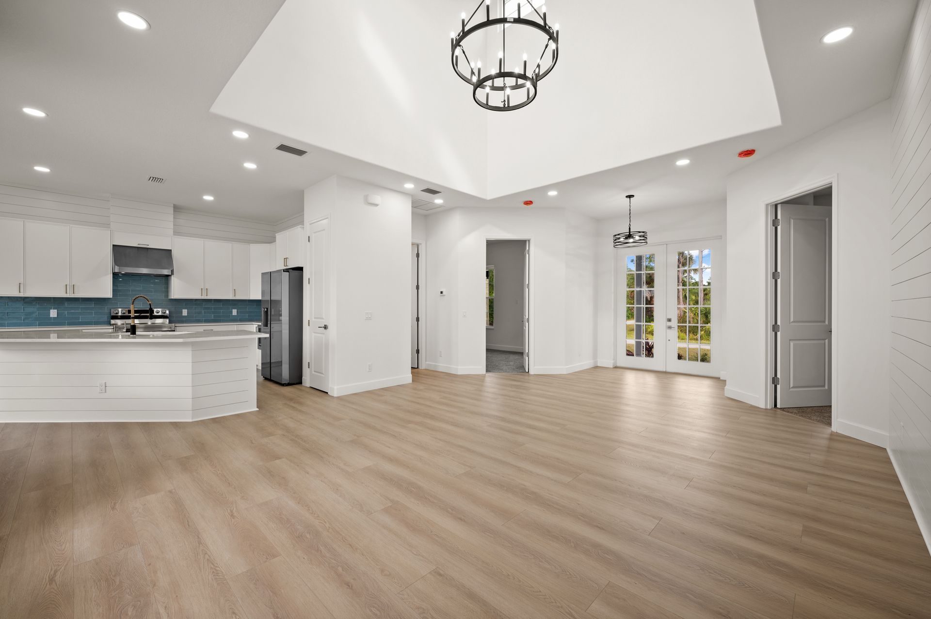 Bright, open-concept living space with a kitchen on the left, dining area with doors to the outside, and a light wood floor.